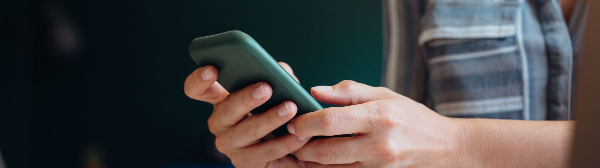 Zwei Hände halten Smartphone auf einem Tisch mit Heft und Kugelschreiber