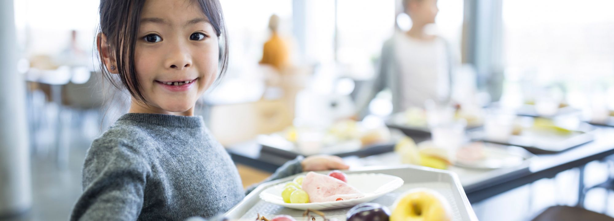 Lächelndes Kind mit Tablett und Essen in einer Mensa