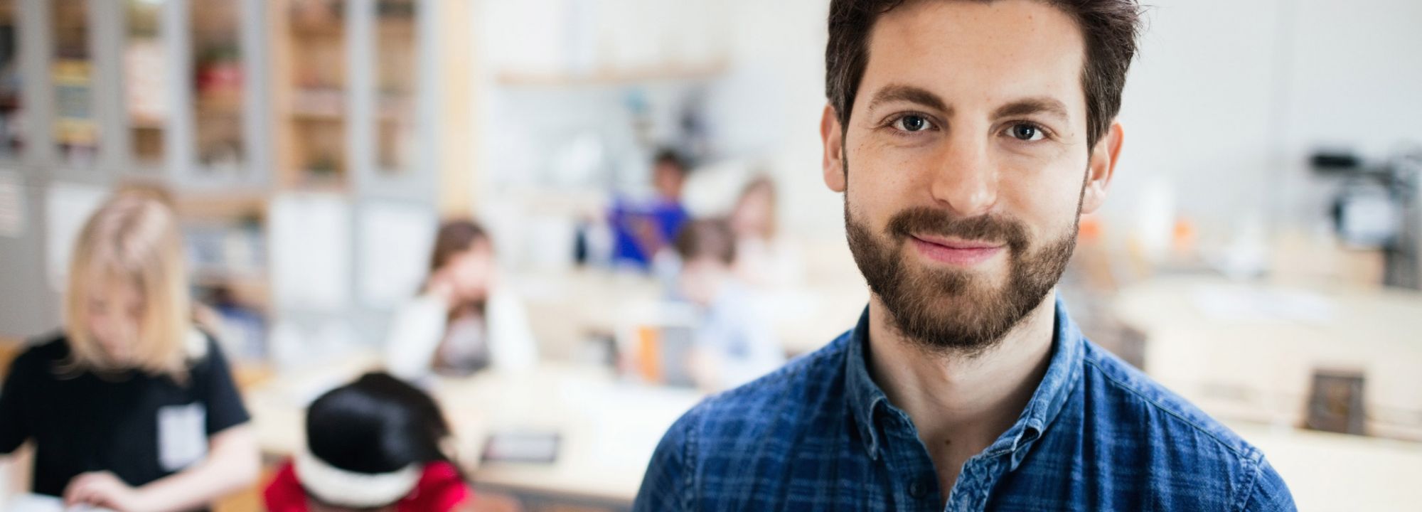 Mann mit BArt und blauem Hemd vor zwei bastelnden Kindern in einem Kreativraum