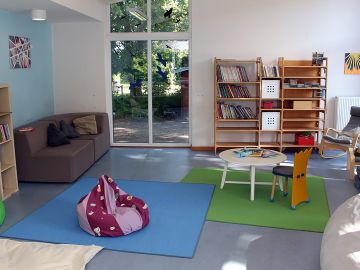 Heller Leseraum mit Sofas, Stühlen, Sesseln, Sitzsäcken, bunten Teppichen und Bücherregalen in der Nachmittagsbetreuung der OGGS Harksheide in Norderstedt