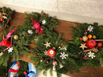 Mehrere Adventskränze mit Tannengrün roten Kerzen Schneeflocken Weihnachtskugeln und goldenen Sternen auf einem braunen Holztisch in der BEB der OGGS Harksheide Nord in Norderstedt