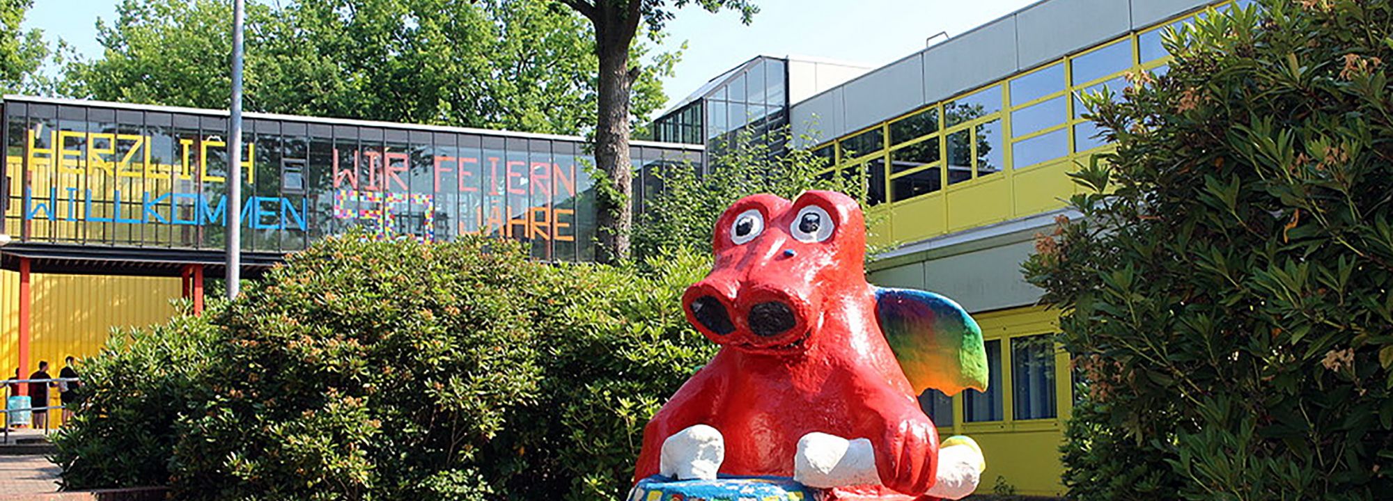 Roter trommelnder Drache als Maskottchen vor dem Schulzentrum Süd in Norderstedt bei Sonnenschein