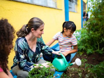Zwei Kinder und eine Frau kümmern sich um ein Hochbeet vor Hauswand